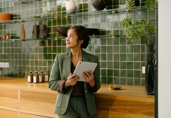 Businesswoman in green suit holding tablet checking indoor climate in modern hotel setting.