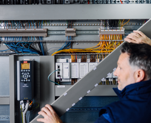 Installer working on Priva BlueID BMS panel with colored wires in a building management system cabinet.