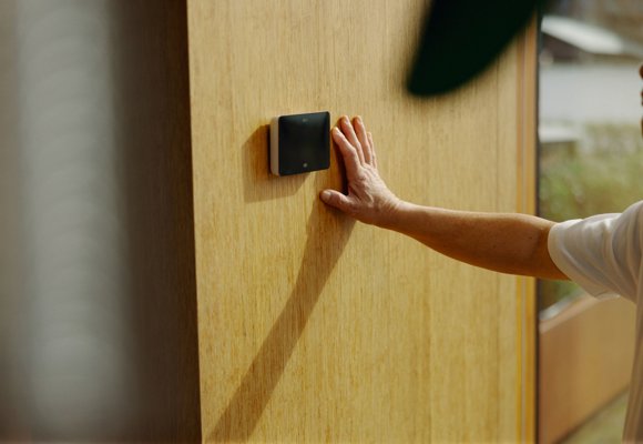 person adjusting indoor climate settings on priva touchpoint 1: A person adjusts a wall mounted climate control device.